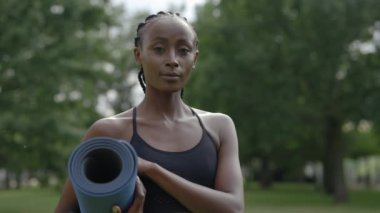 Parkta yoga minderiyle duran Afrikalı Amerikalı kadın.