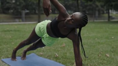 Afro örgülü spor kadın parkta yoga yapıyor.