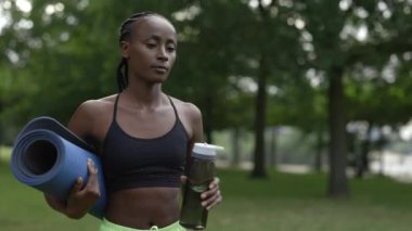 Green Park 'ta su şişesi ve yoga minderi taşıyan bir kadın.