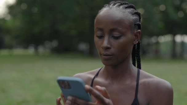 Woman with braids using mobile while resting during training — Stockvideo