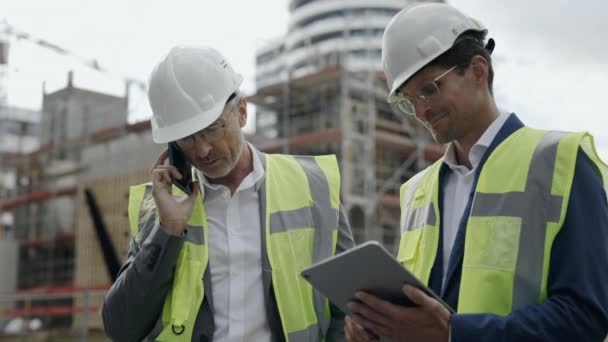 Two engineers using tablet and mobile on construction site — Stockvideo