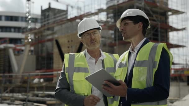 Hombres en cascos de seguridad usando tableta en el sitio de construcción — Vídeos de Stock