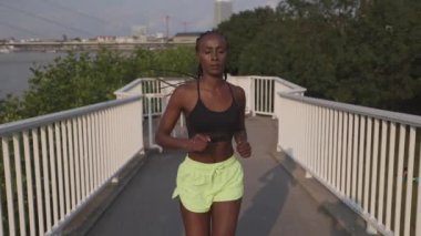 Şehir köprüsünde koşan spor elbiseli aktif bir kadın.