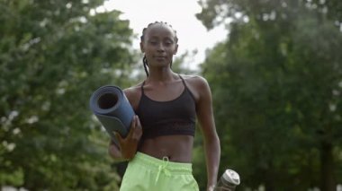 Dışarıda yoga minderiyle dikilen Afro-Amerikan portresi.