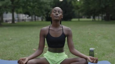 Yoga minderinde oturan ve parkta meditasyon yapan kadın.