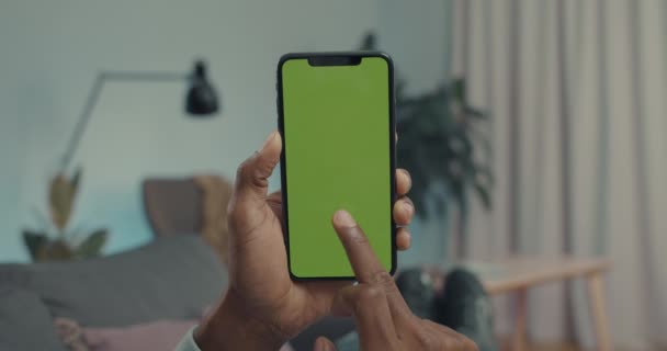 Lviv, Ukraine - October 20, 2021: African american man tapping with forefinger on chroma key screen of modern smartphone. Male person lying on couch and holding cell phone in horizontal position. — Video Stock