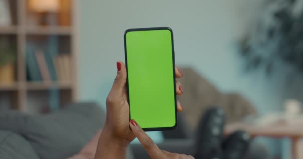 African american woman sliding with forefinger on green screen of modern smartphone. Close up of female hands holding cell phone. Copy space. — 图库视频影像