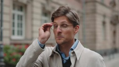 Orta yaşlı bir adam gözlük takıp kameraya bakıyor.