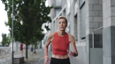 Aktif kıyafetli yaşlı bir kadın dışarıda koşuyor.