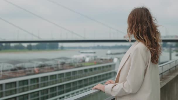 Ώριμη γυναίκα στέκεται στη γέφυρα και ψάχνει στο ποτάμι της πόλης — Αρχείο Βίντεο