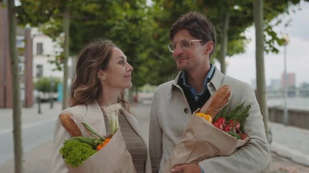 Pasangan tersenyum di depan kamera dan memegang tas belanjaan di luar ruangan — Stok Video