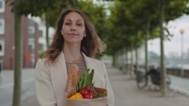 Market poşetiyle sokakta poz veren olgun kadın portresi.