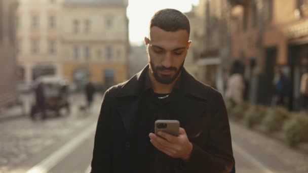 Hombre de negocios árabe usando el móvil mientras camina por la calle — Vídeos de Stock