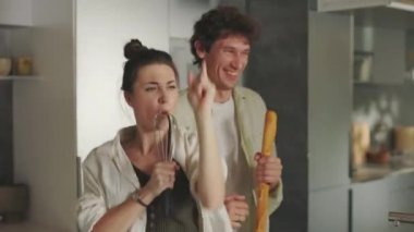 Birbirine aşık iki insan mutfakta dans edip şarkı söylüyor.