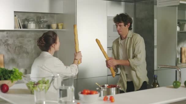 Zabawny mężczyzna i kobieta mając walkę z bagietki w kuchni — Wideo stockowe