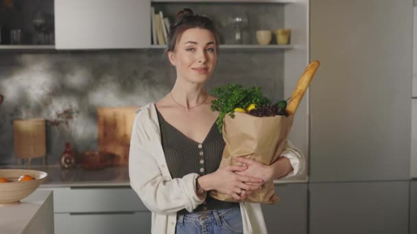 Woman standing on kitchen and holding bag with food — Stockvideo
