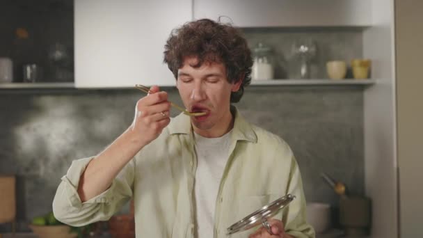 Человек пытается приготовить еду из ложки, стоя на кухне — стоковое видео