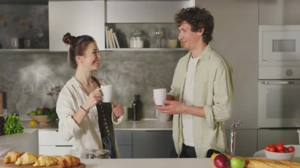 Любящая пара целуется и пьет кофе на кухне — стоковое видео
