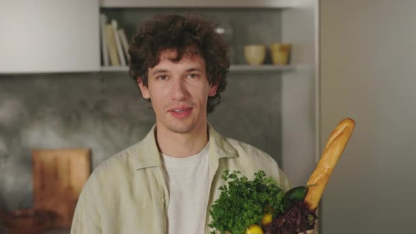 Красивый мужчина, стоящий на кухне с пакетом продуктов — стоковое видео