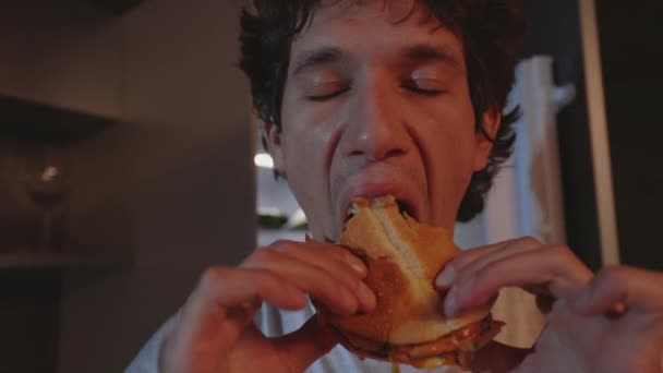 Éhes ember áll a konyhában, és eszik hamburgert éjszaka — Stock videók