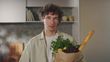 Mutfakta elinde alışveriş torbasıyla duran beyaz bir adam.