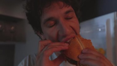 Kafkasyalı bir adam geceleri buzdolabının yanında hamburger yiyor.