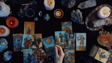 New York, ABD - 1 Mayıs 2021: Kimliği belirsiz genç bir kadın, karanlık odanın içindeki oturumda kart okurken mumlarla birlikte tarot kartlarını masaya koyuyor. Mistisizm ve okültizm kavramı.
