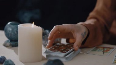 New York, ABD - 1 Mayıs 2021: Falcı kadın kameraya mumla kart gösteriyor ve masadaki diğer şeyler tarot kartıyla tahmin ediyor. Astroloji ve okültizm kavramı,