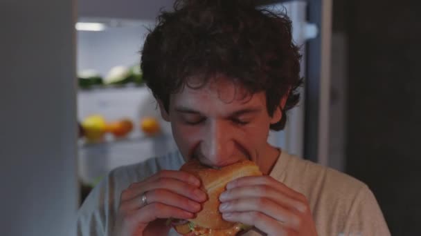 Girig man äter hamburgare på köket på natten — Stockvideo