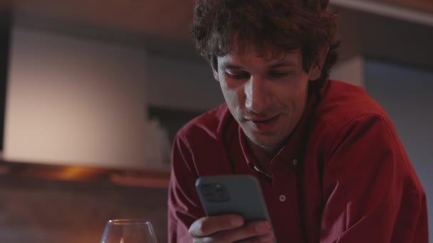 Positiv mann som chatter på mobil og drikker vin hjemme – stockvideo