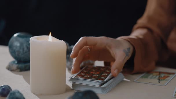 New York, USA - 2021. május 1.: Fortune Teller kártyát mutat a kamerának, miközben tarot kártyákat helyez el, és varázslatot szór rájuk. Asztal gyertyákkal. Megjövendölés és mágia, ezoterikus fogalom. — Stock videók