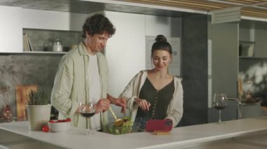 Kadın ve erkek mutfakta yemek pişiriyor ve akıllı telefon kullanıyor.