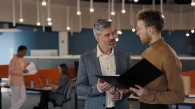 İş merkezinde yan yana duran ve ortak projeyi tartışan iki erkek arkadaş. Meslektaşlar kahve içiyor, elinde belgelerle klasörü tutuyor ve dijital tablet kullanıyor..