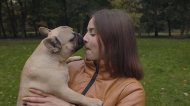 Fransız bulldog 'u parkta burnunu yalarken gülümseyen kadın.
