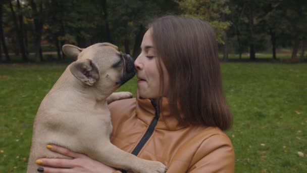 Wanita tersenyum saat bulldog Perancis menjilati hidungnya di taman — Stok Video