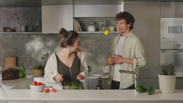 Pareja feliz divirtiéndose mientras cocina ensalada en la cocina — Vídeo de stock