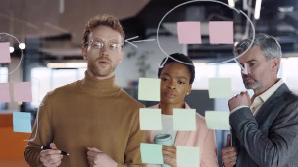 Diverse group of finance office worker having corporate training and using glass board. Young man office worker standing and writing on glass wall an talking with his colleagues. — Stock Video