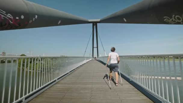 DUSSELDORF, NÉMETORSZÁG - 2021. július 1.: A Düsseldorfban, Németországban található, a Rajna feletti modern hídnál skandináv sétáló női személy mozgáskamerája. Nagy nyári nap. — Stock videók