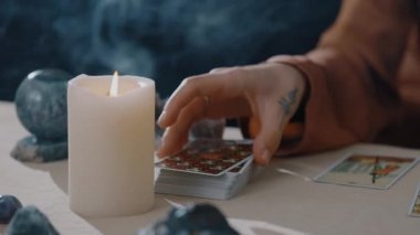New York, ABD - 1 Mayıs 2021: kehanet ve sihir. Falcı, tarot kartlarını dağıtıyor ve onlara büyü yapıyor. Kameraya kart gösteren ellerin yakın çekimi. Mumlu masa. Esrarengiz kavram.