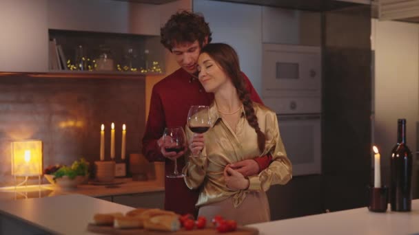 Άντρας με ένα ποτήρι κρασί αγκαλιάζει γυναίκα στην κουζίνα — Αρχείο Βίντεο