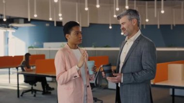 Modern ofiste çeşitli dost canlısı iş arkadaşları konuşuyor. Gülümseyen erkek ve kadın ofis çalışanları koridorda durup iş arasında bir şey tartışıyorlar..