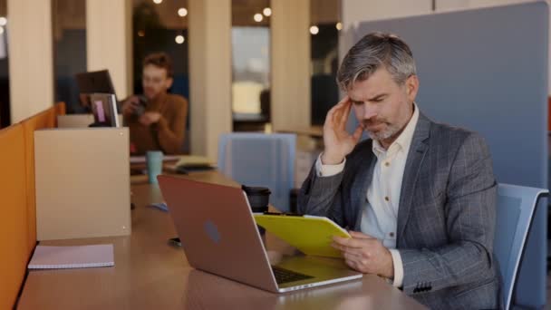 Portrait d'un homme d'affaires caucasien travaillant sur un ordinateur portable dans le bureau ayant un terrible mal de tête pendant les heures de travail. Overworker et concept de santé. — Video