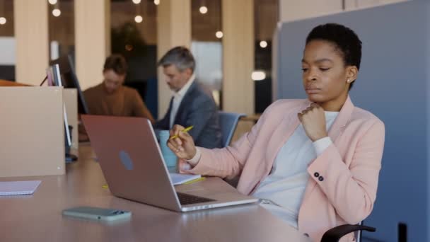 Mujer joven afroamericana que trabaja en la computadora portátil sentada en cómodamente oficina con sus colegas en el fondo. Negocios, trabajo, concepto freelance. — Vídeos de Stock