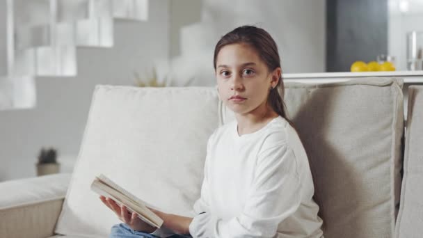 Porträtt av kvinnlig tonåring sittande på soffan med bok i handen — Stockvideo