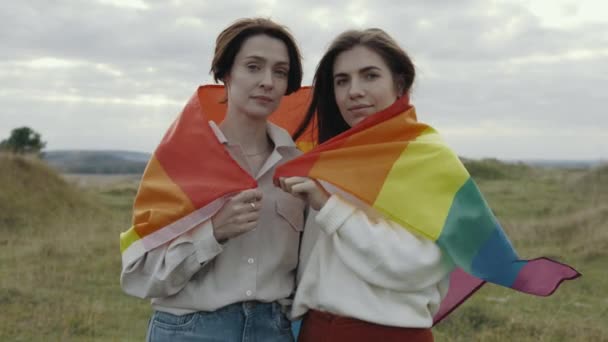 Две любящие женщины с радужным флагом lgbt позируют на природе — стоковое видео