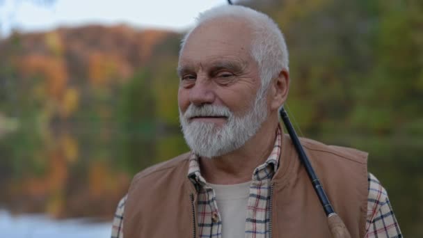 Uomo anziano in posa vicino lago con canna da pesca in mano — Video Stock
