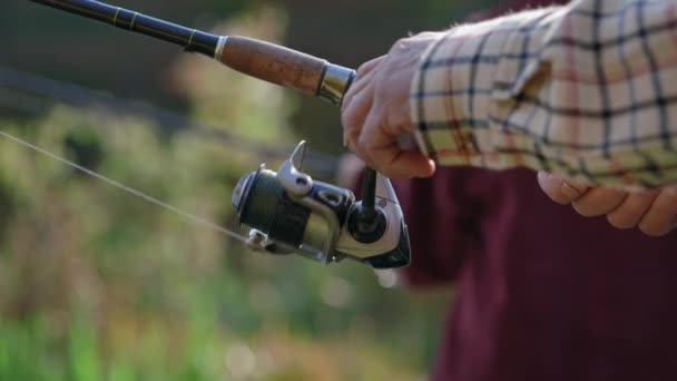 Nahaufnahme der Angelrute mit Spule in den Händen eines gealterten Anglers — Stockvideo