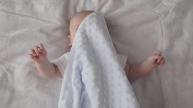 Yeni doğmuş erkek bebek battaniyeyle örtülmüş olarak yatakta yatıyor.