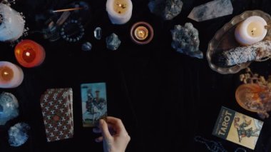 New York, ABD - 1 Mayıs 2021: Kadın falcının karanlık odada müşterinin önünde otururken tarot kartlarını masaya koyması. Sihirli pagan kaderi okuma ritüeli.