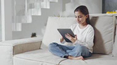 Güzel liseli kız kanepede dinleniyor ve dijital tablet kullanıyor